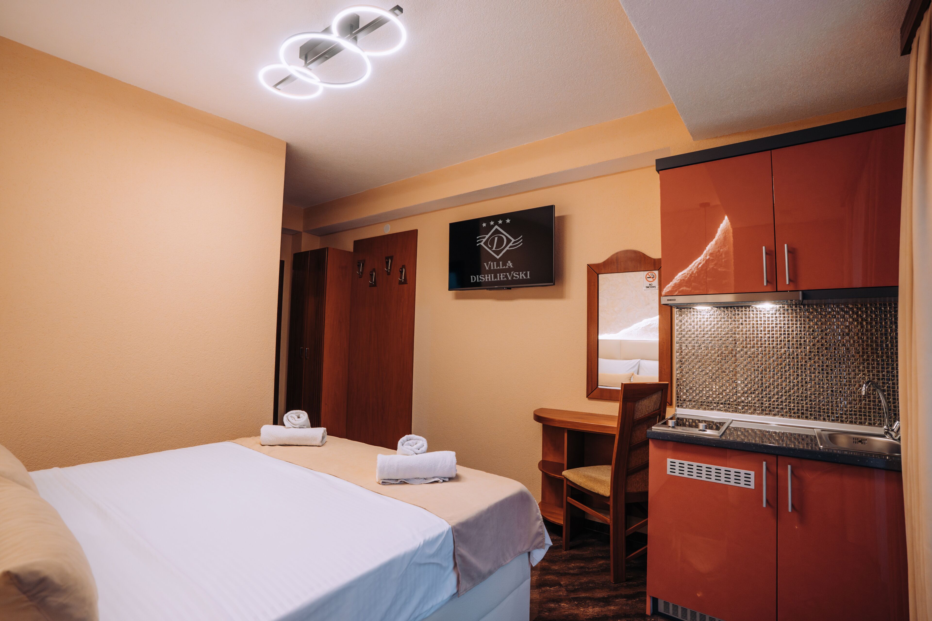 A hotel room with a bed, a desk, a mirror, and a kitchenette.