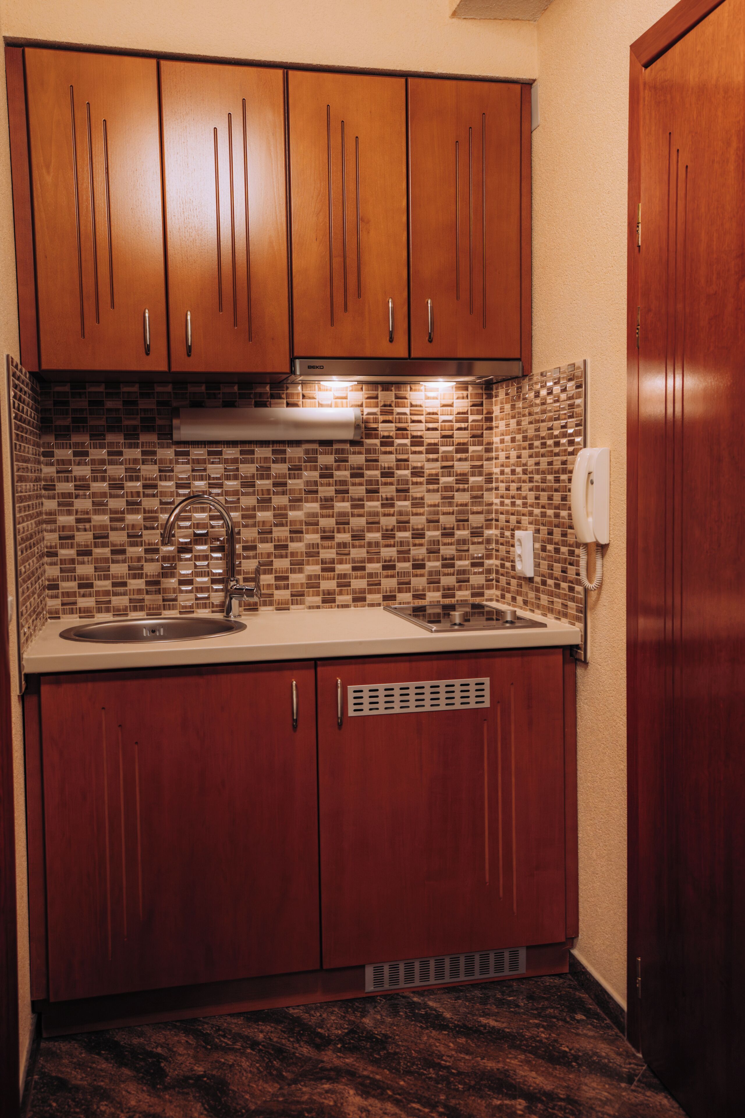 Een keuken met houten kastjes, een roestvrijstalen spoelbak, een betegelde spatwand en een inbouw afzuigkap.