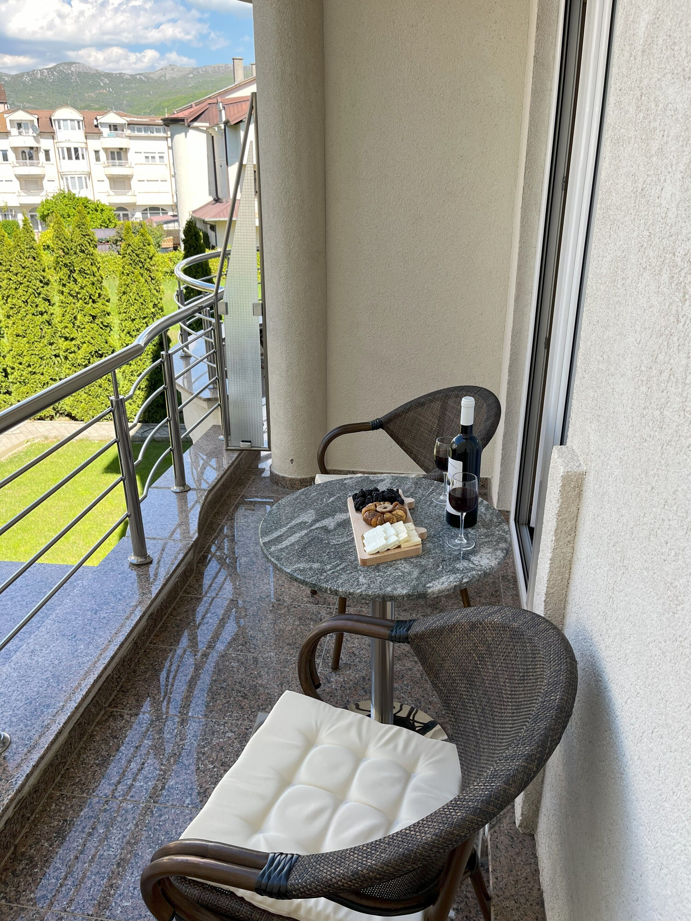 A balcony with a table, chairs, a bottle of wine, and a cheese board.