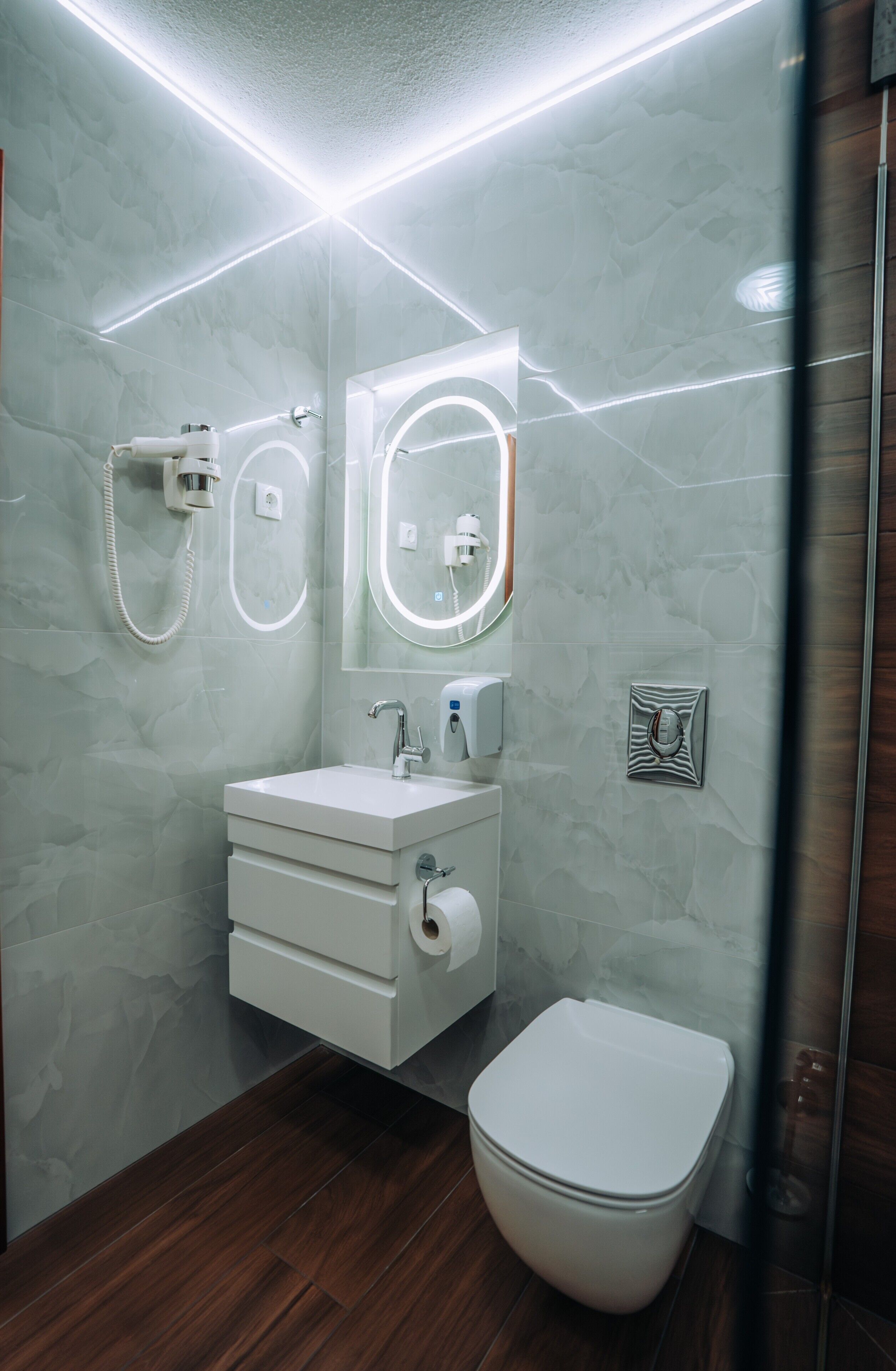 Un baño moderno con pared de mármol, un lavabo blanco, un espejo, un inodoro y una ducha.