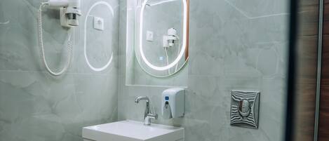 Un baño moderno con pared de mármol, un lavabo blanco, un espejo, un inodoro y una ducha.