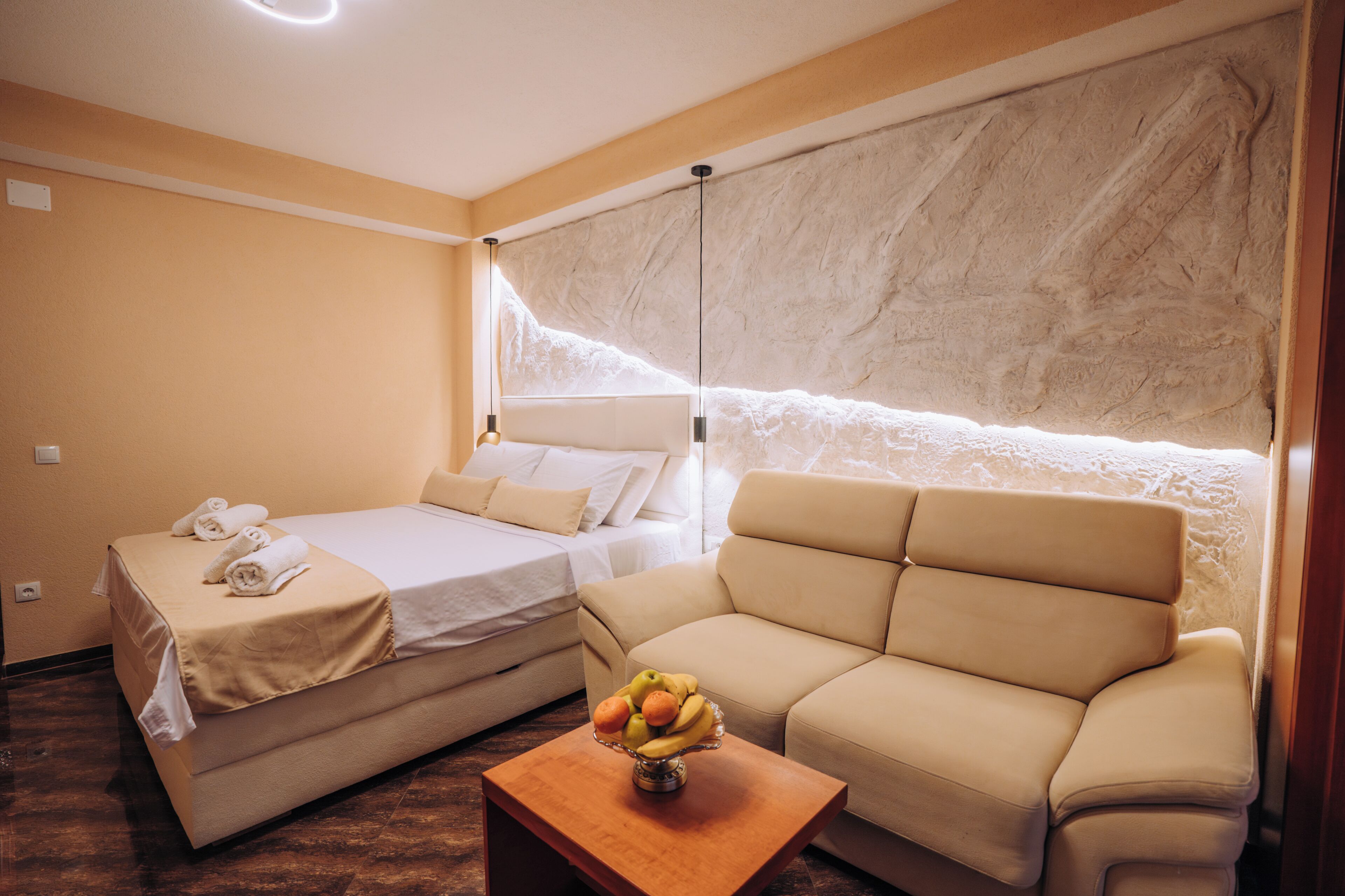 Une chambre d’hôtel avec un lit, un canapé, une petite table avec des fruits et un mur au décor texturé.