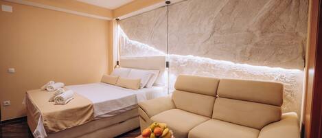 Une chambre d’hôtel avec un lit, un canapé, une petite table avec des fruits et un mur au décor texturé.