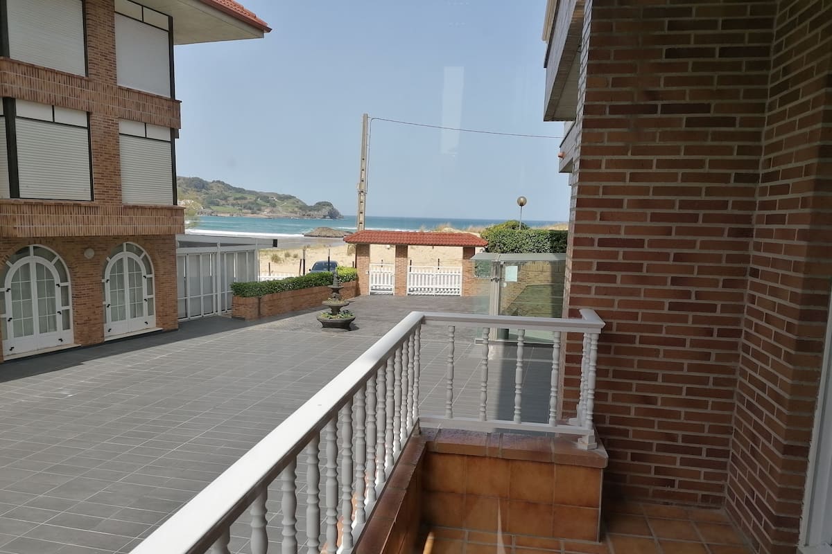 A balcony with a white balustrade, a brick wall, and a view of the sea and hills in the background.