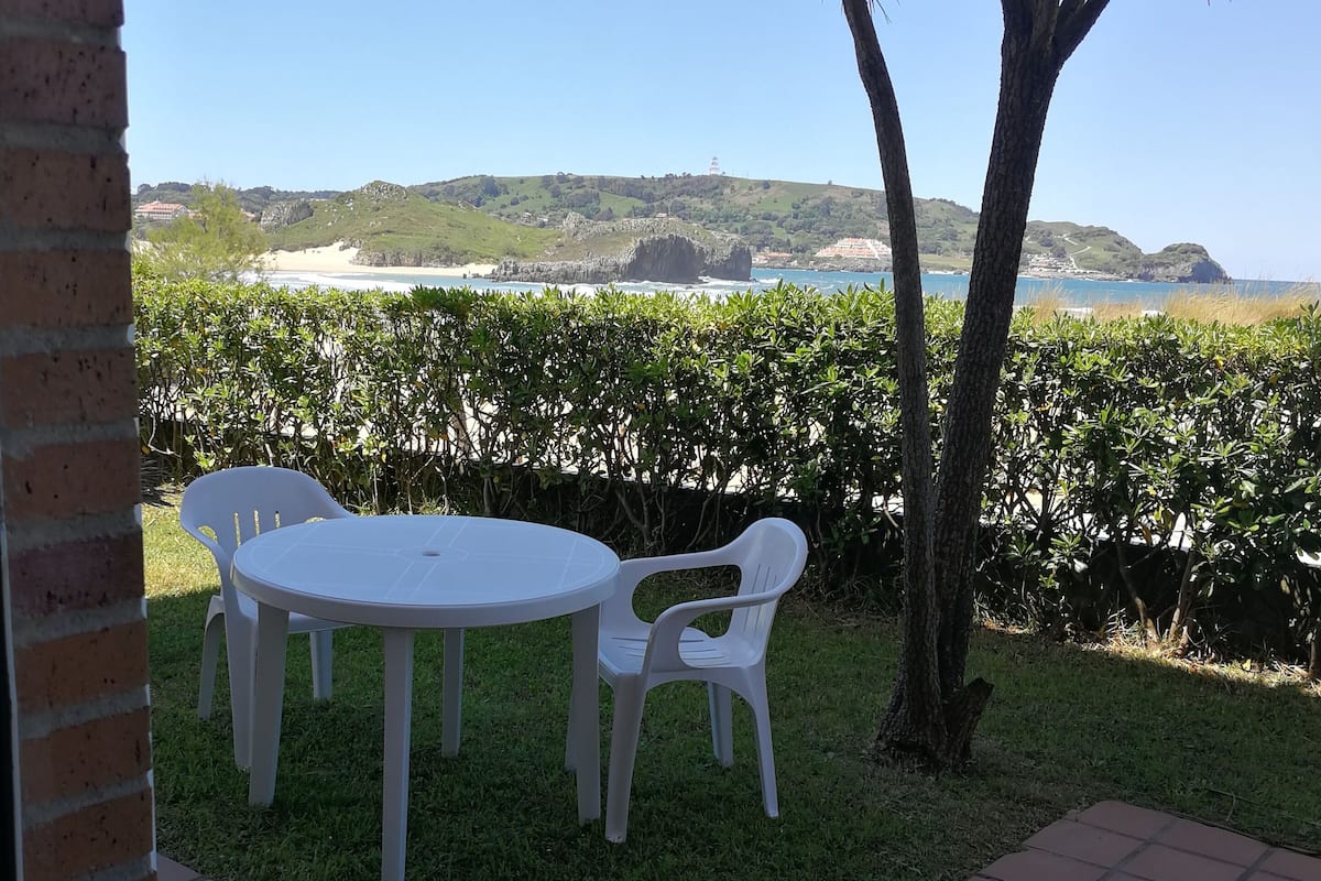 A patio with a white table and chairs, a brick wall, and a view of the beach and hills.