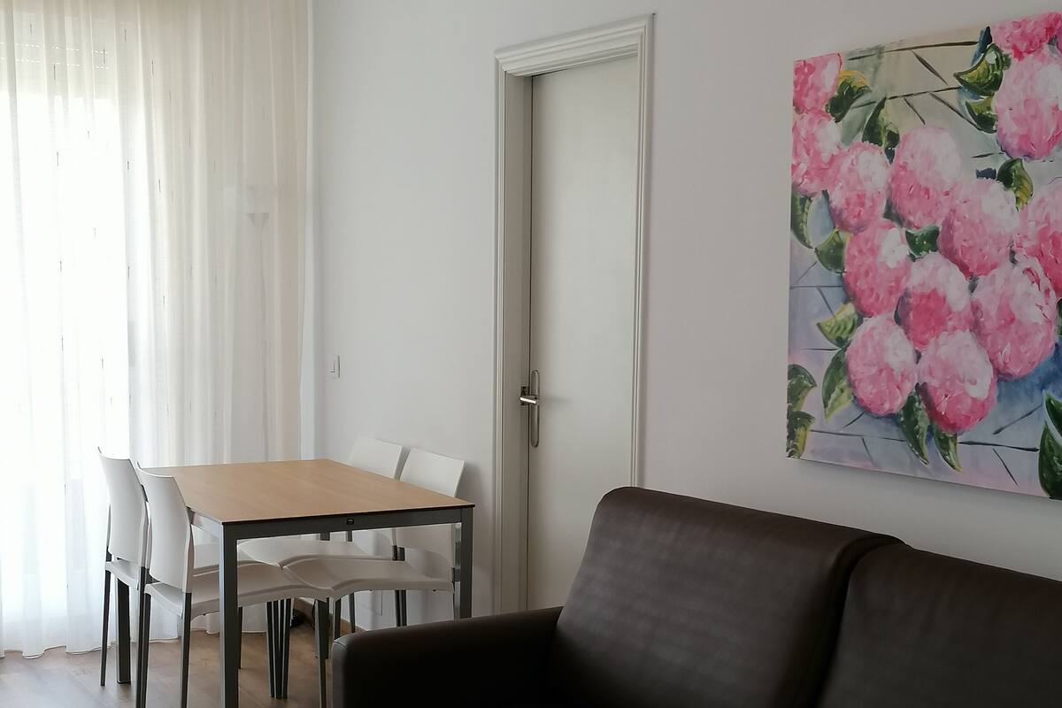A living room with a brown sofa, a dining table with chairs, and a door.