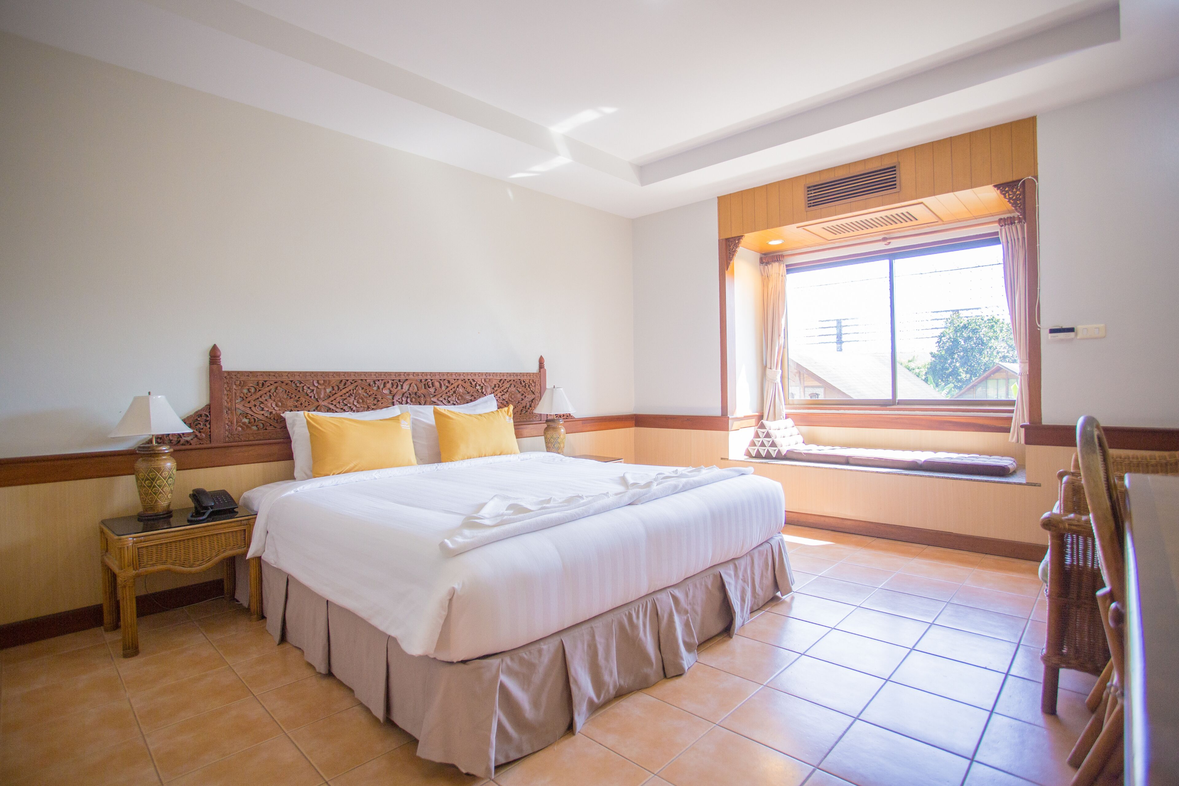 A hotel room with a large bed, a bedside table with a lamp, a window with curtains, and a view of the outside.