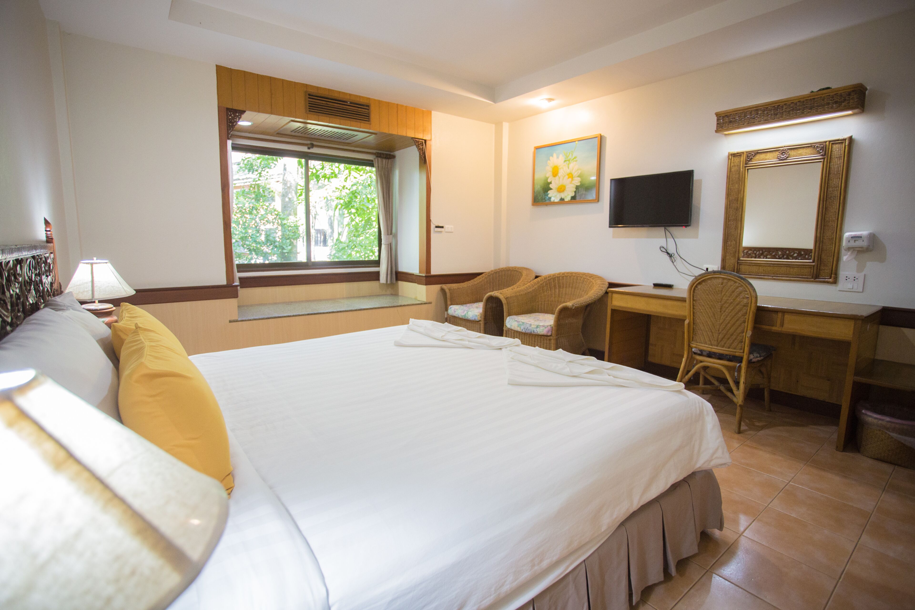 A hotel room with a large bed, a desk, a chair, a television, and a window with curtains.