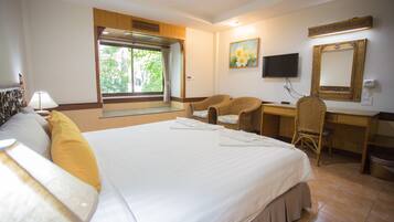 A hotel room with a large bed, a desk, a chair, a television, and a window with curtains.