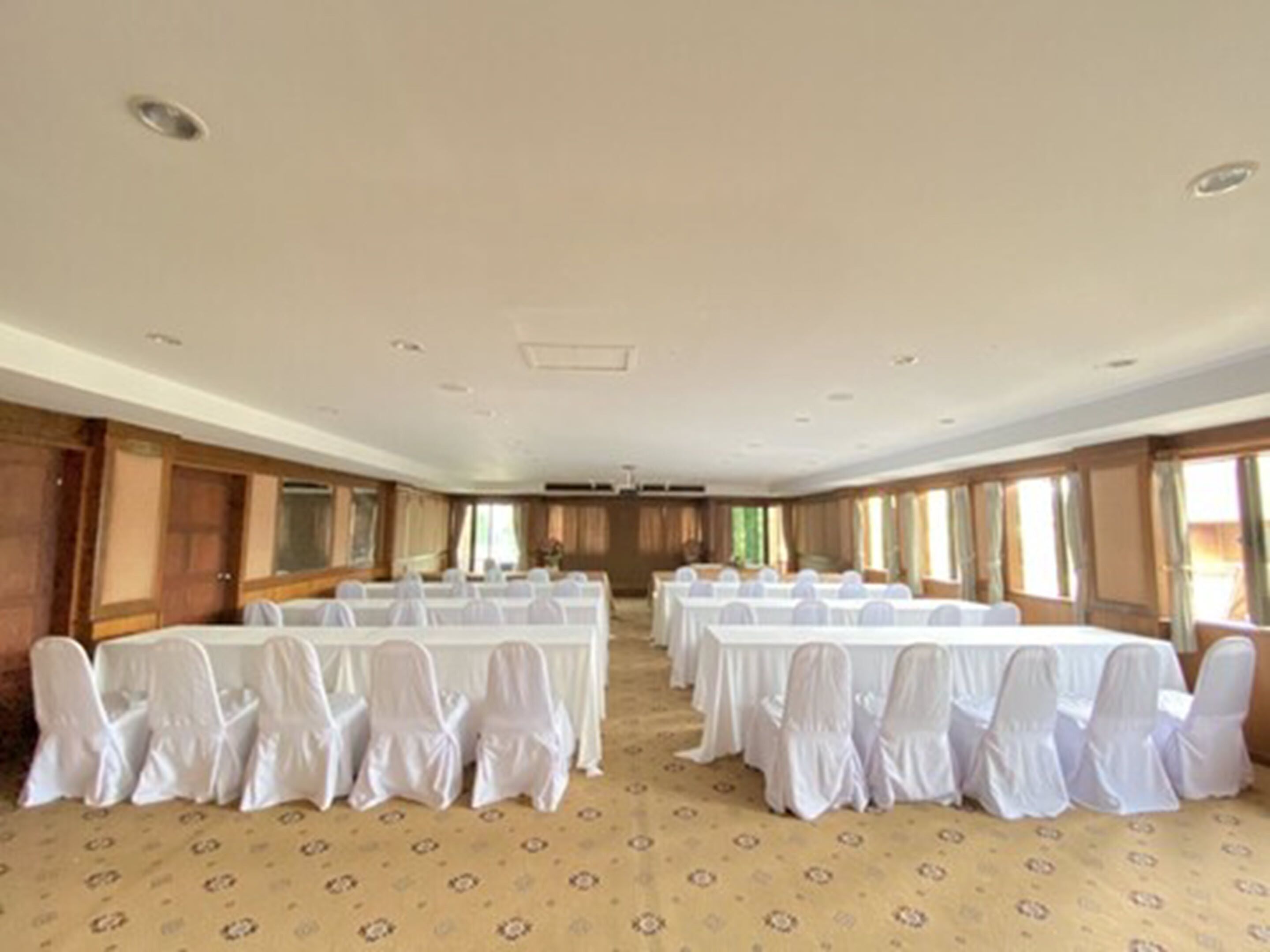 A large conference room with multiple tables and chairs, wooden paneling on the walls, and large windows.