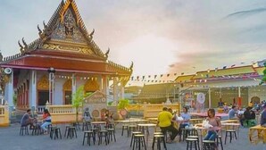 Un espacio de comedor al aire libre con mesas y sillas, un edificio tradicional con arquitectura ornamentada, y un cielo despejado.