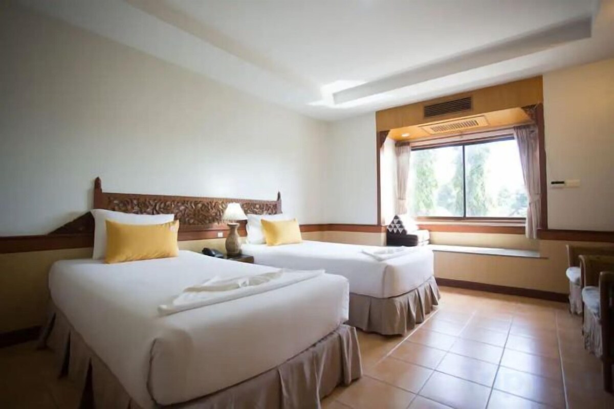 A hotel room with two beds, a window with curtains, and a ceiling vent.