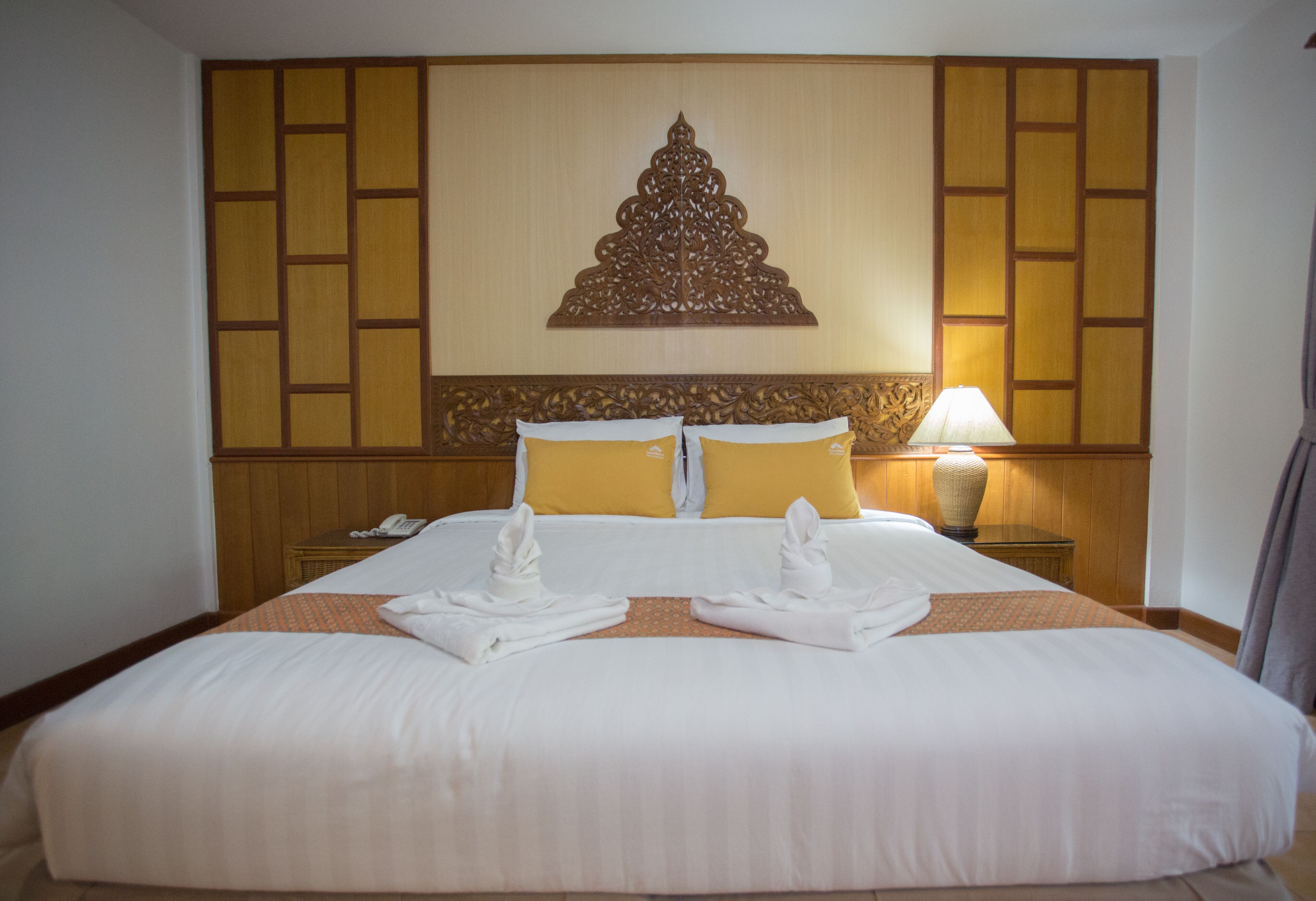 Habitación de hotel con una cama grande, dos almohadas, una mesita de noche con lámpara y un panel decorativo en la pared.