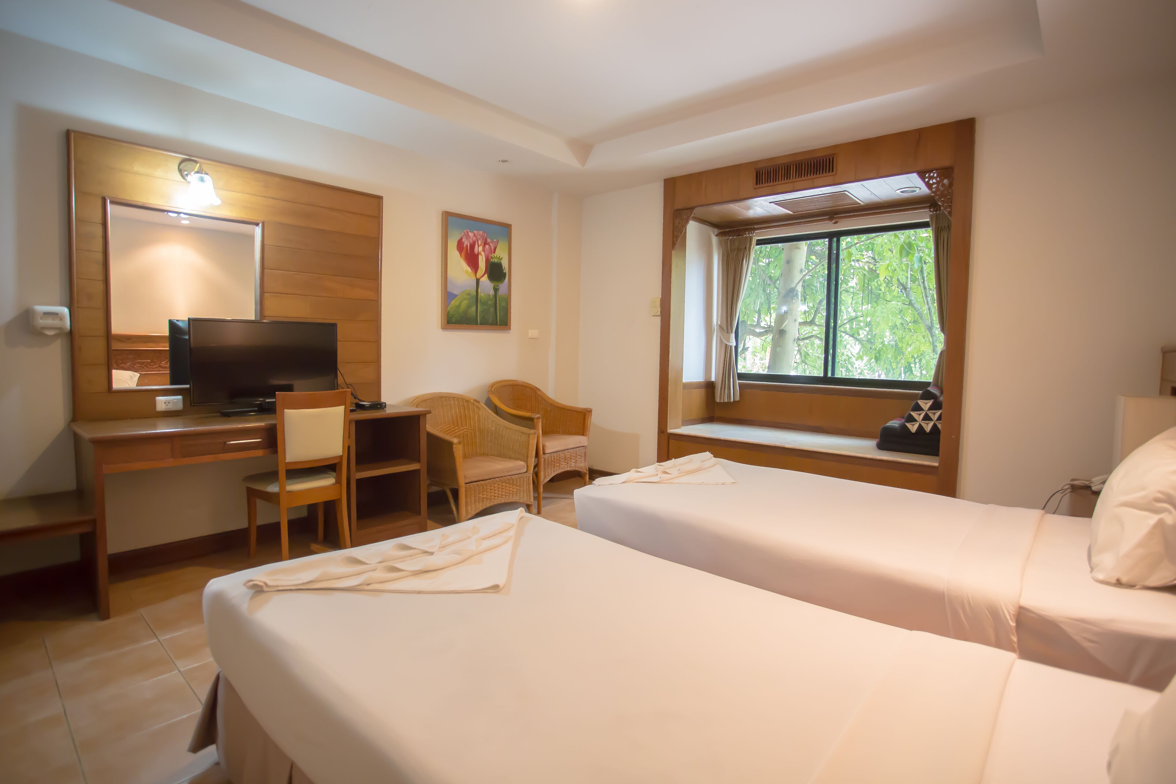 A hotel room with two beds, a desk with a TV, a chair, and a window with a view of trees.