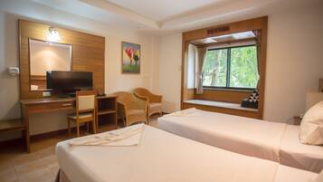 A hotel room with two beds, a desk with a TV, a chair, and a window with a view of trees.