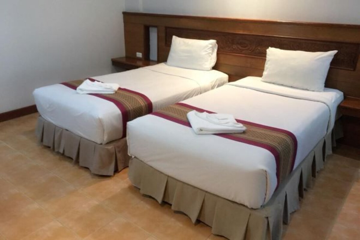 Une chambre d’hôtel avec deux lits simples, chacun doté d’une tête de lit en bois, de draps blancs et d’une base recouverte d’un tissu.