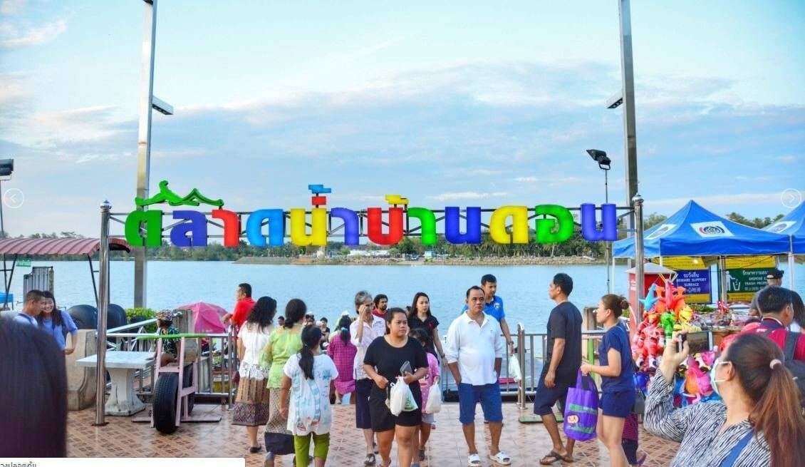 A group of people standing in front of a colorful sign with Thai script.