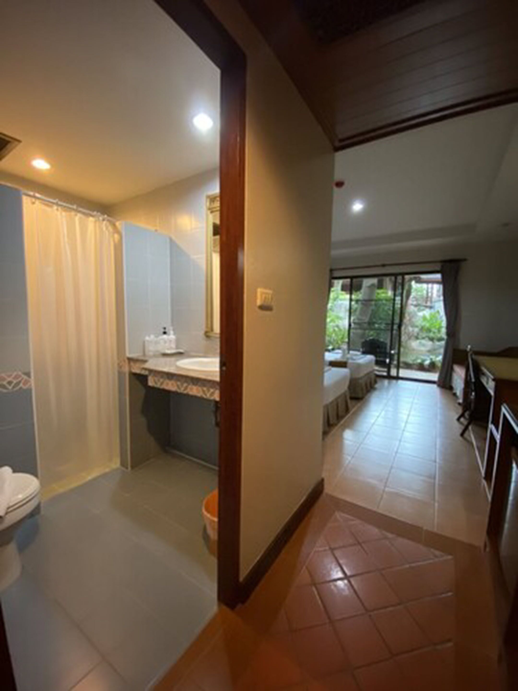 A bathroom with a shower, toilet, and sink. There is a window with a view of greenery outside.