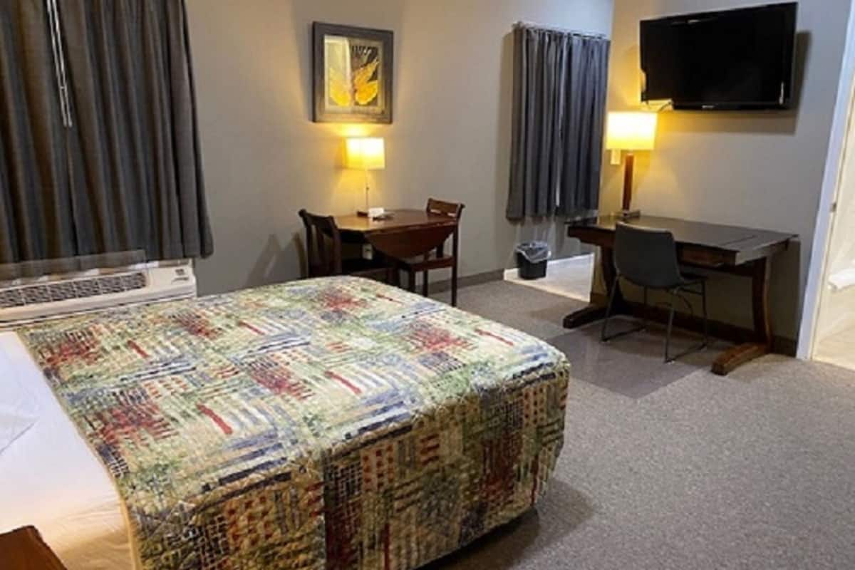 Quarto de hotel com cama, escrivaninha, cadeira, televisão e um quadro na parede.