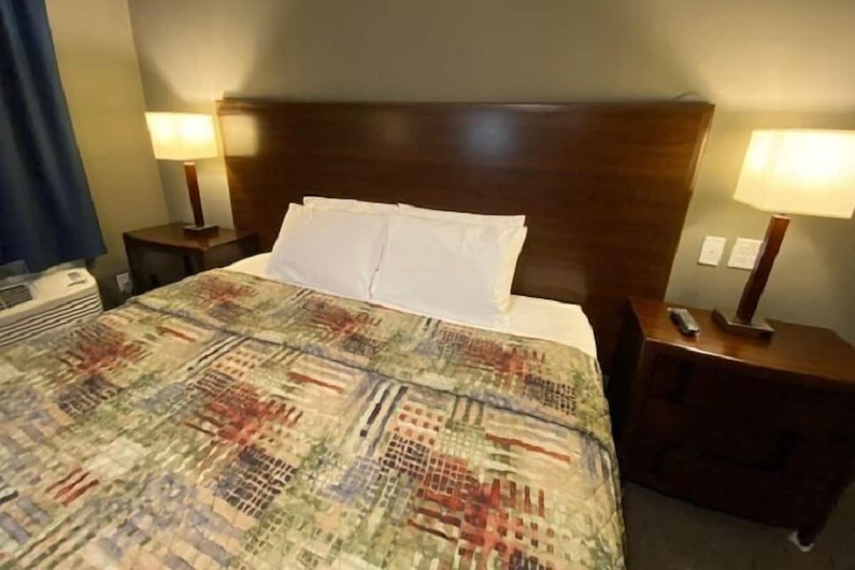 Quarto de hotel com uma cama grande, duas mesas de cabeceira com luminárias, aquecedor fixado na parede e uma janela com cortinas.