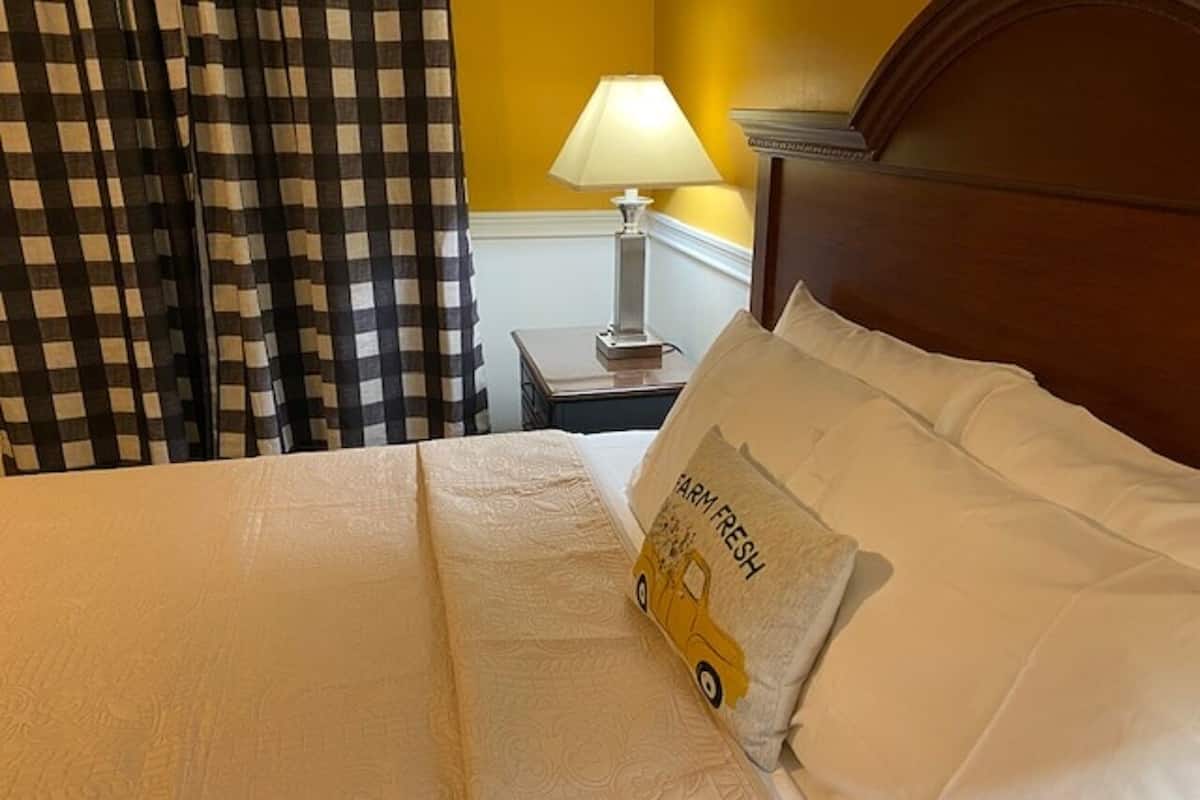 Uma cama bem arrumada com uma almofada de design rústico e um tema de fazenda, uma cortina xadrez e um abajur.