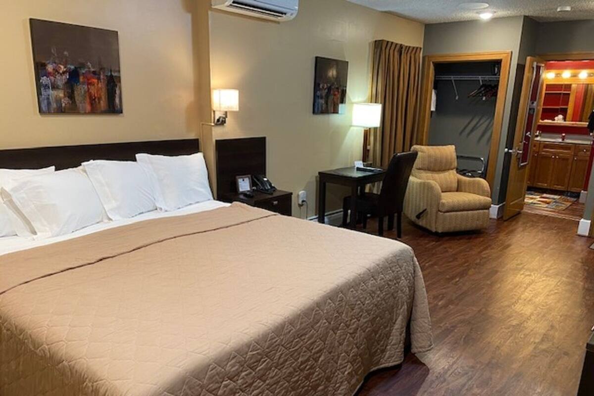 Quarto de hotel com uma cama grande, uma escrivaninha, uma cadeira e um banheiro visível através de uma porta aberta.