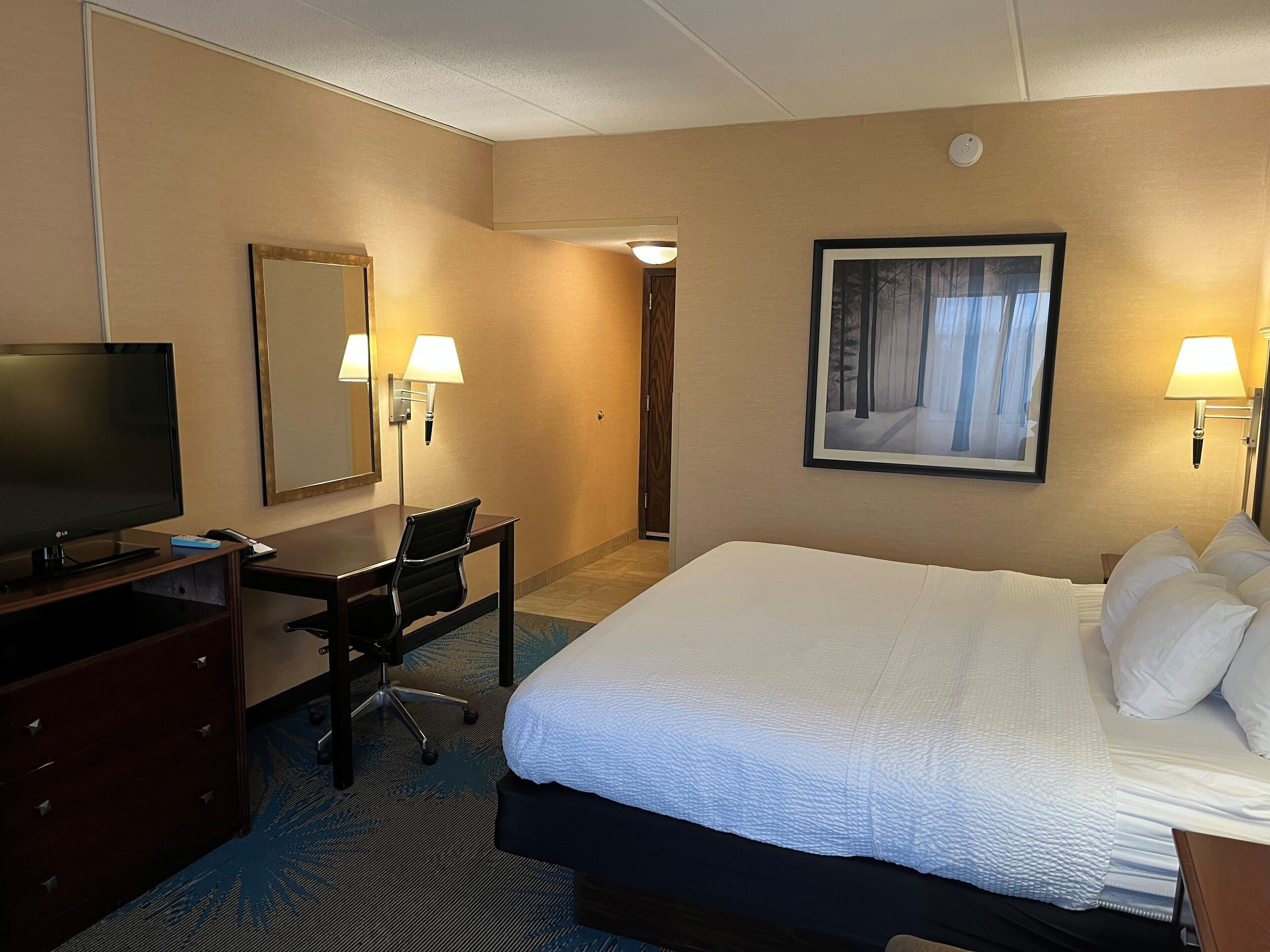 Habitación de hotel con una cama grande, un escritorio con silla, un televisor y dos lámparas de pared.