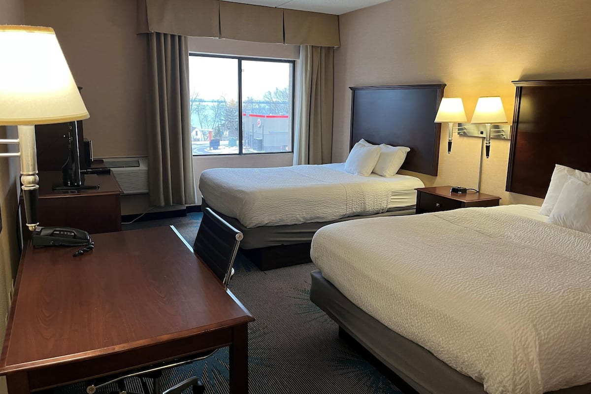 A hotel room with two beds, a desk, a telephone, and a window with curtains.
