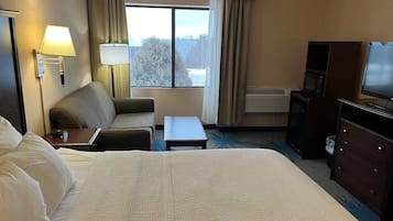 A hotel room with a large bed, a sofa, a small table, a TV, and a desk with a lamp.