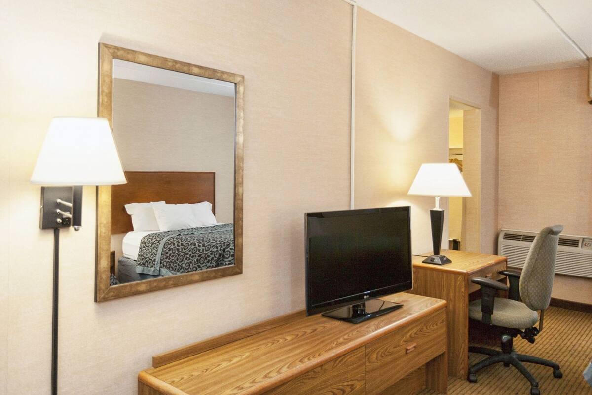 A hotel room with a bed, a TV on a wooden desk, a chair, a desk lamp, and a mirror.