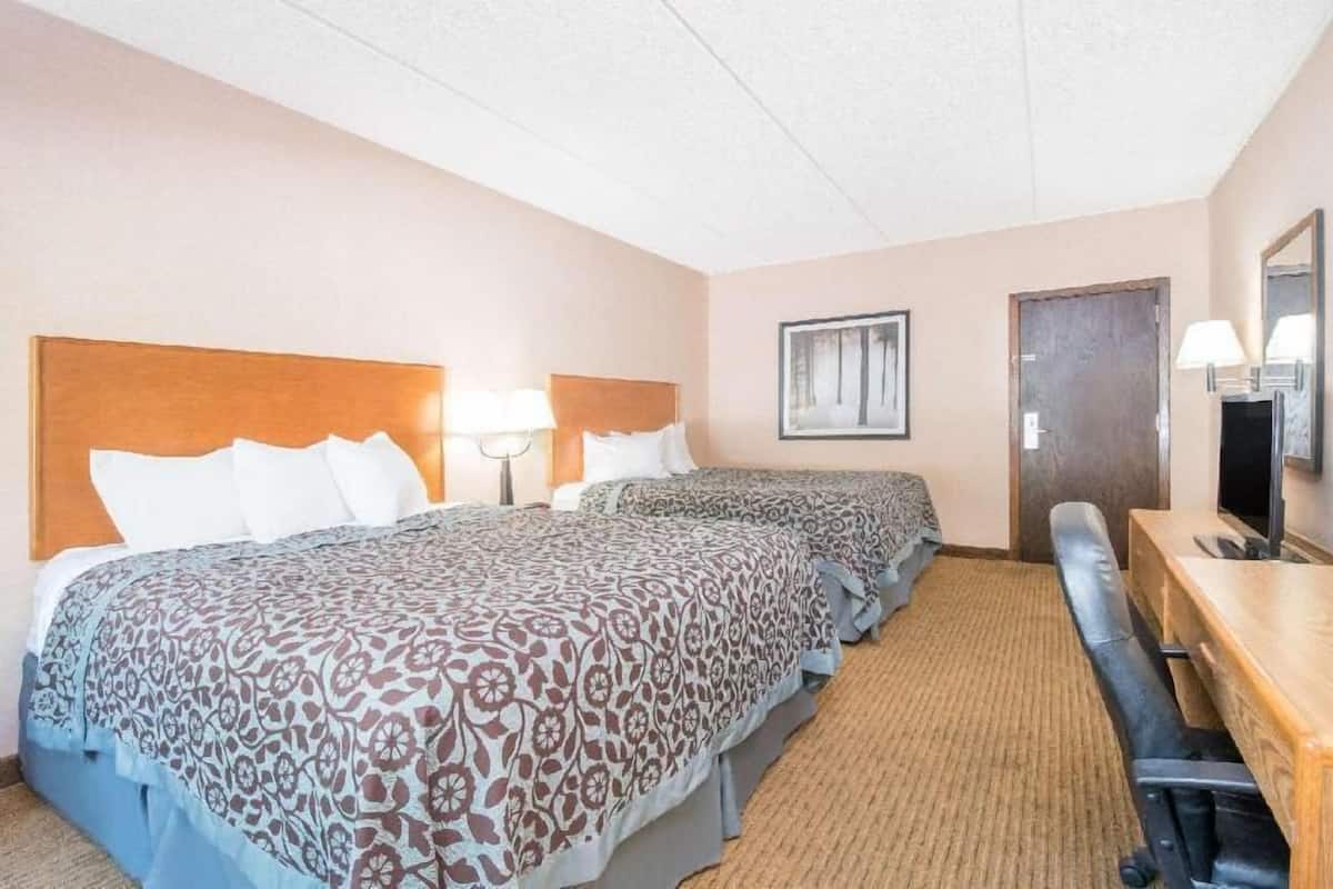 A hotel room with two beds, a desk, a chair, a TV, and a door.