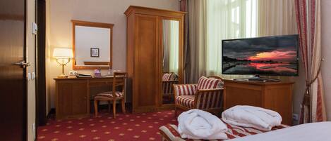 A hotel room with a bed, a desk with a lamp, a TV, a chair, and a wardrobe.