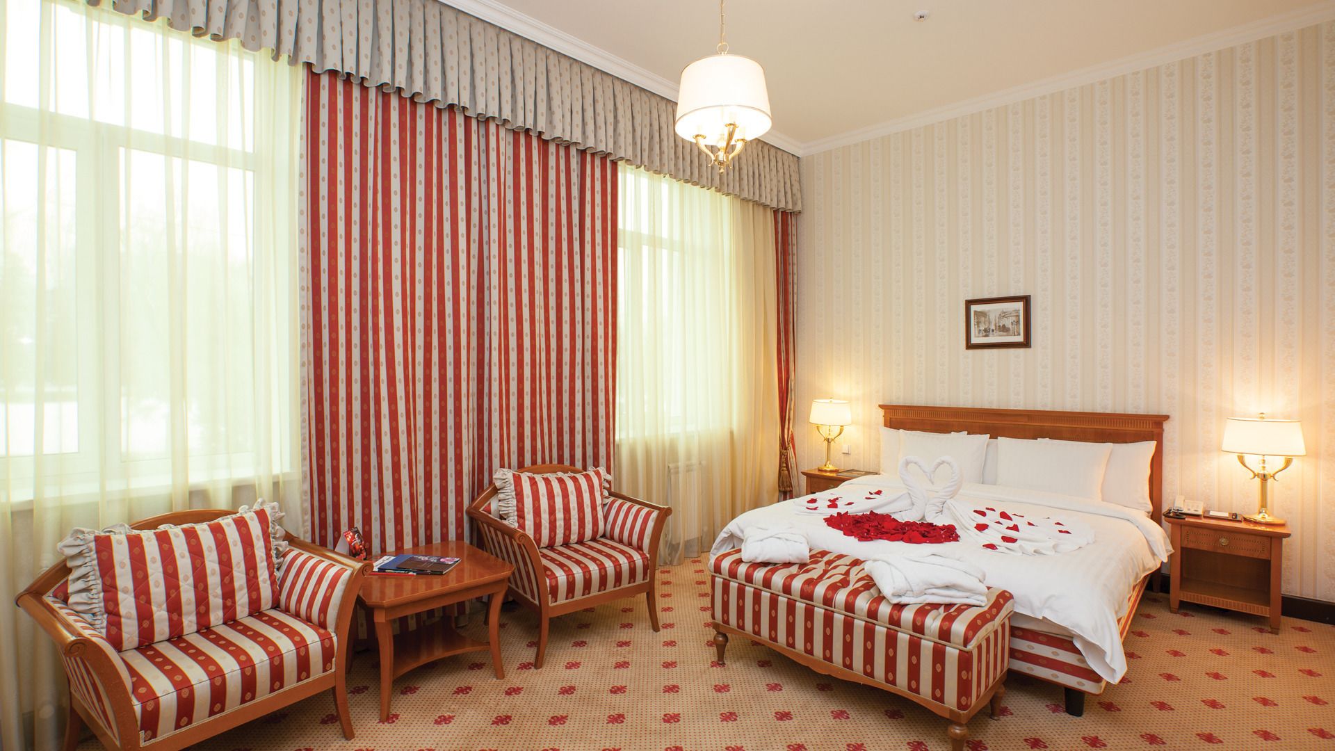 A hotel room with a large bed, two armchairs, a small table, and a nightstand with lamps.