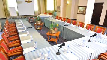 Un salón de conferencias con mesas largas, sillas, micrófonos y botellas de agua.