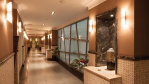 A hotel corridor with a long hallway, wall sconces, a large mirror, and potted plants. - Grand Hotel Tien Shan (Almaty)