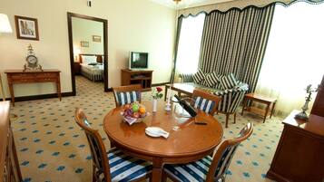 A hotel room with a round dining table, striped sofa, and a television.