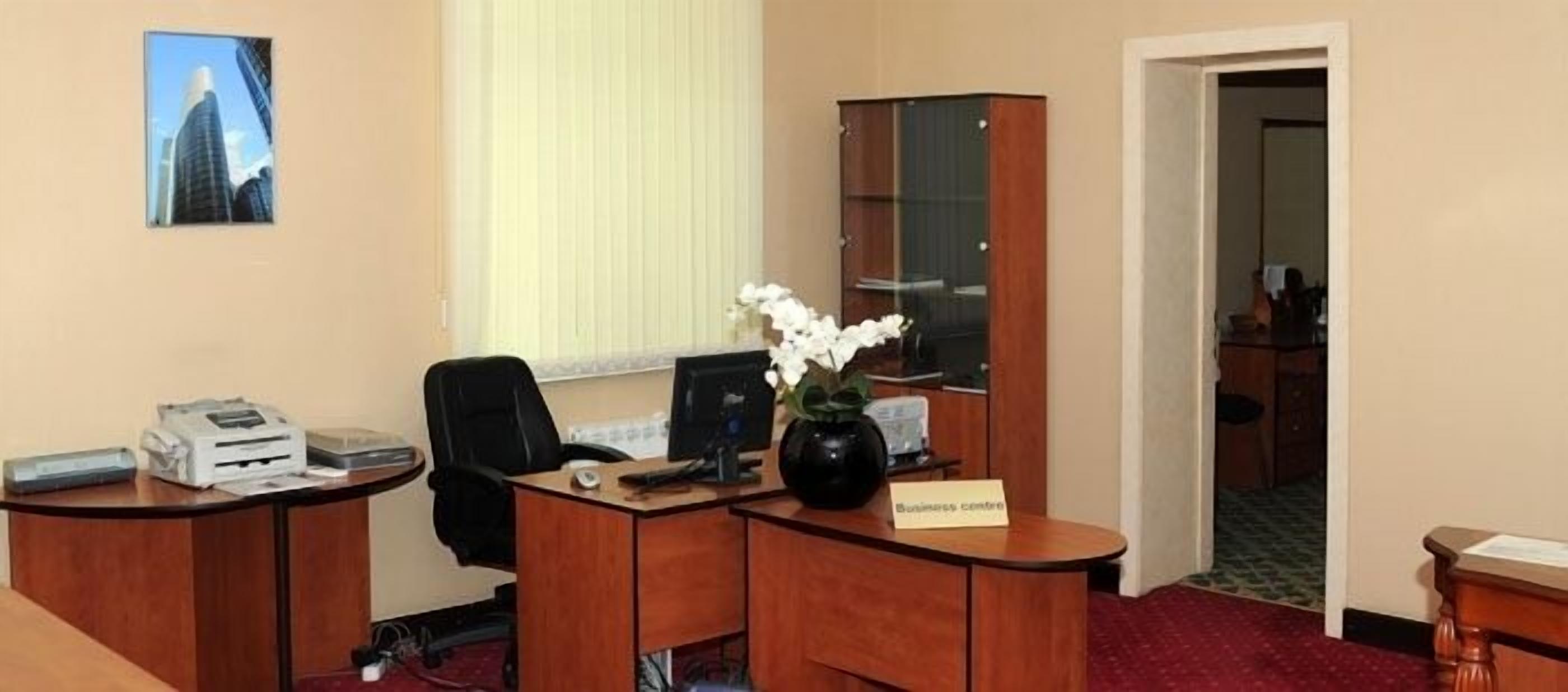 Un centre d’affaires équipé d’un bureau, d’un ordinateur, d’une imprimante et d’un vase avec des fleurs blanches.