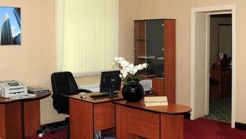 Un centre d’affaires équipé d’un bureau, d’un ordinateur, d’une imprimante et d’un vase avec des fleurs blanches.