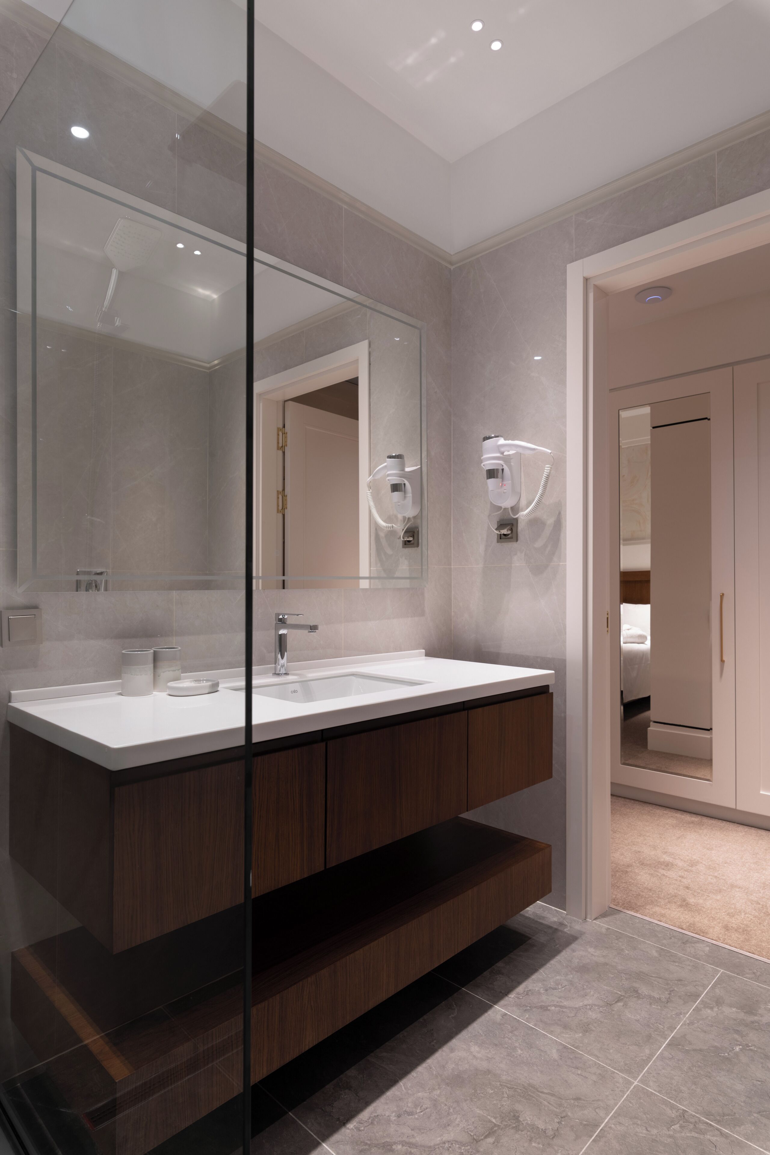 Un baño moderno con un espejo grande, lavamanos dobles y un separador de vidrio.