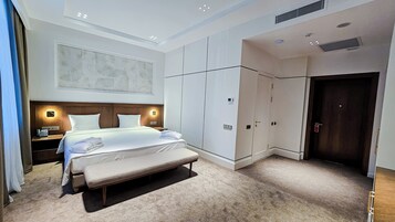 Una habitación de hotel moderna con una cama grande, un banco, un armario y una puerta.