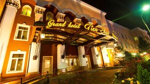 A grand hotel entrance with a prominent illuminated sign, a covered entrance, and a well-maintained garden area. - Grand Hotel Tien Shan (Almaty)