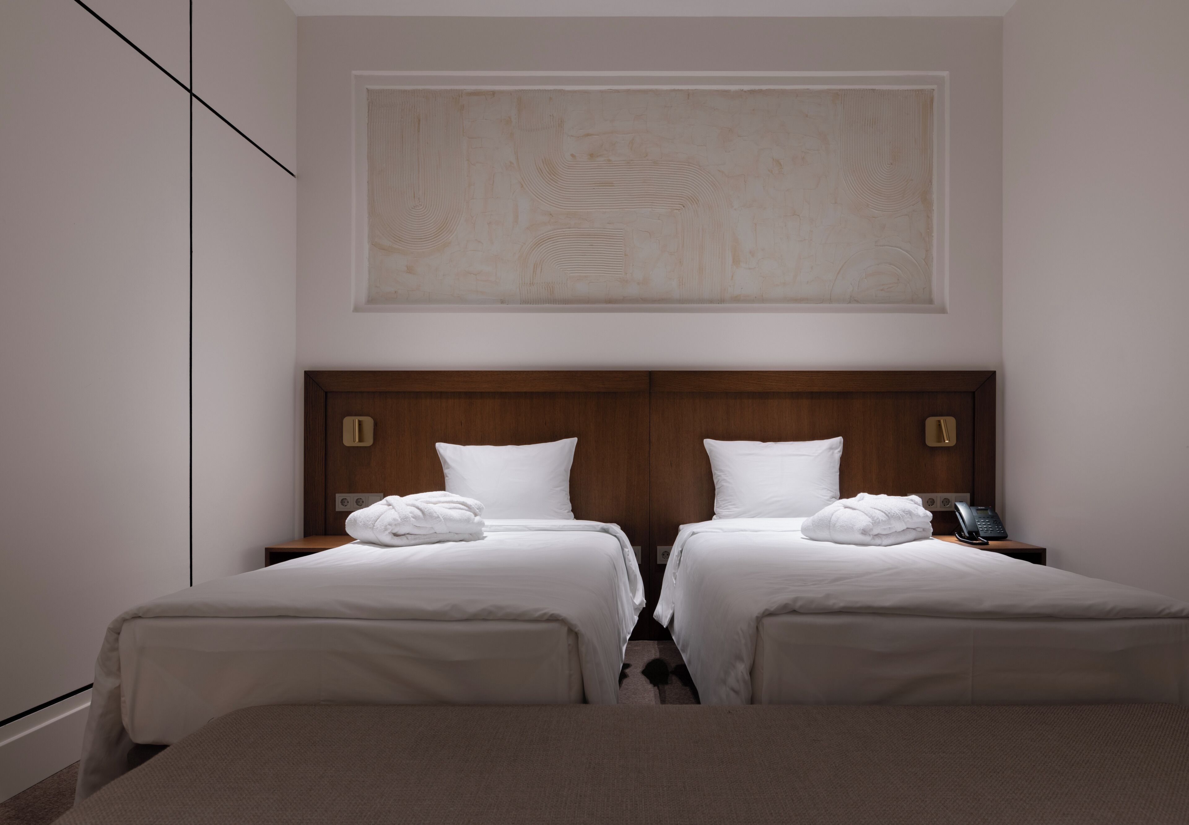 A hotel room with two beds, a wooden headboard, a large abstract painting, and a bedside phone.