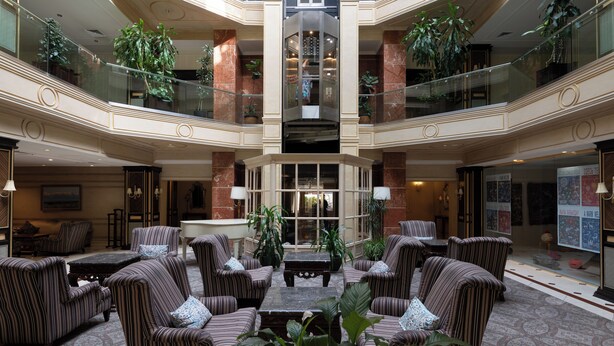 A spacious lobby with a central seating area, multiple levels with glass railings, and numerous potted plants. - Grand Hotel Tien Shan (Almaty)