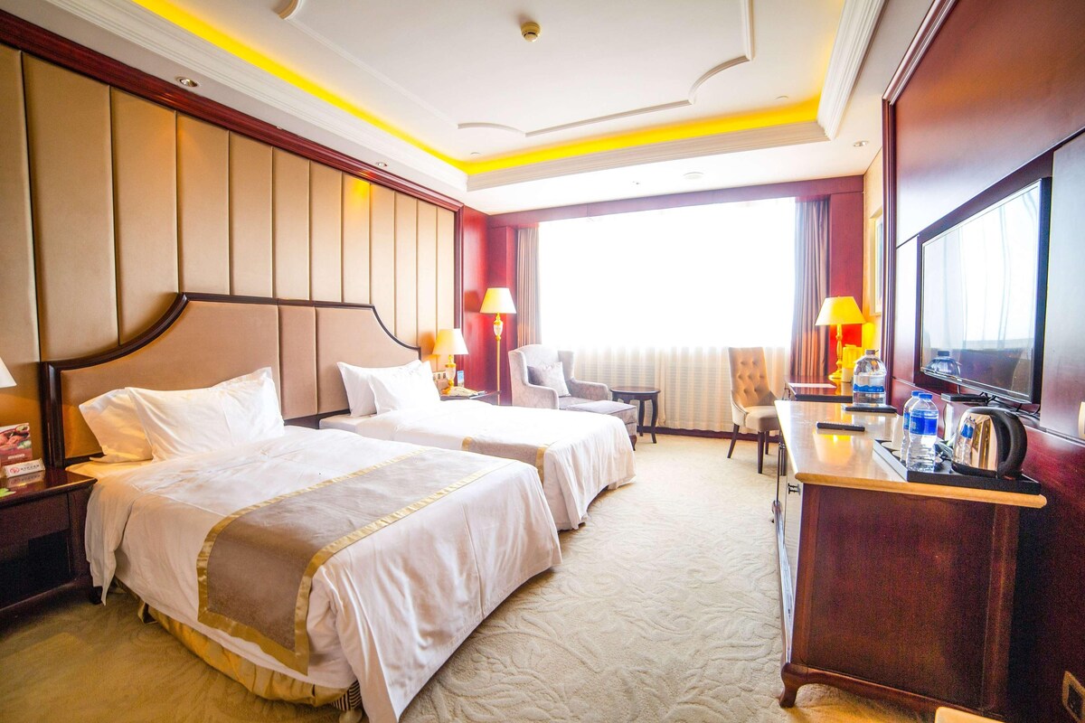 Habitación de hotel con dos camas, un escritorio con televisor y una ventana con cortinas.