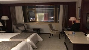 Habitación de hotel con dos camas, un escritorio, una silla y una ventana con vistas a la ciudad.