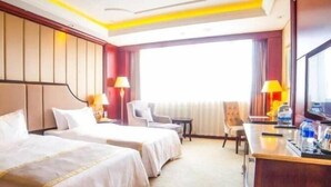 Habitación de hotel con dos camas, un escritorio, una silla, un televisor y un ventanal grande.