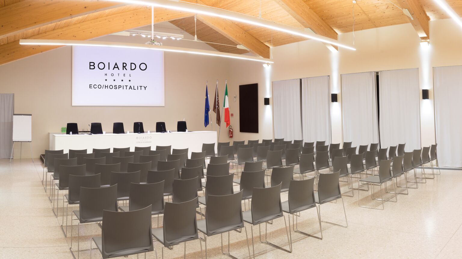 Une salle de conférence avec des rangées de chaises, un pupitre et des drapeaux.