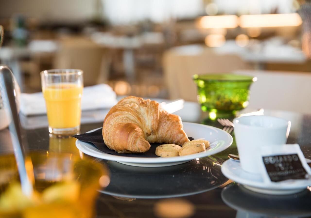 Une table dressée pour le petit-déjeuner, avec des croissants, des biscuits, un verre de jus d’orange et une tasse de café.