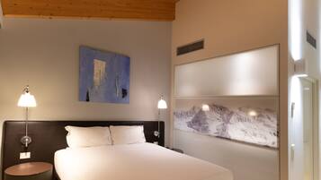 A bedroom with a wooden ceiling, a large bed with white bedding, two bedside tables with lamps, and a wall-mounted artwork.