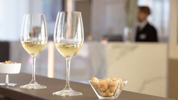Dos copas de vino sobre una mesa, con un cuenco de frutos secos y un postre al fondo.